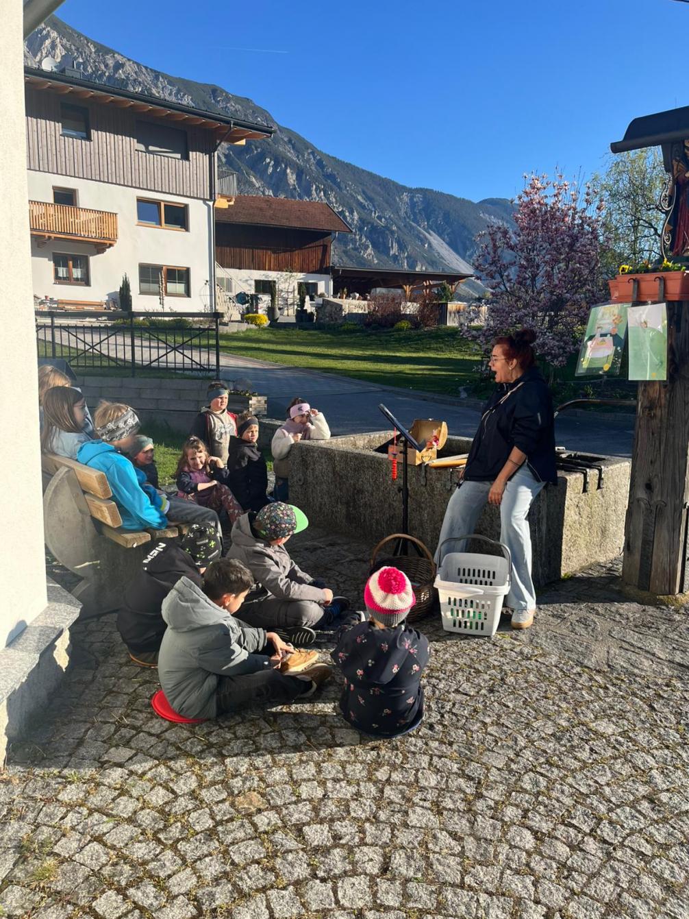 Kinder hören das Märchen vor dem Brunnen