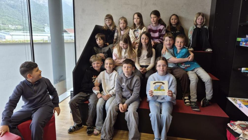Kinder sitzen gemeinsam in der Bücherei und bekommen ein Buch vorgelesen