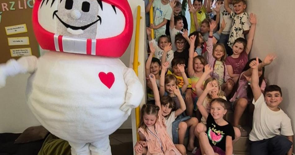 Die ersten Klassen stehen neben dem Helmi-Maskottchen auf der Stiege